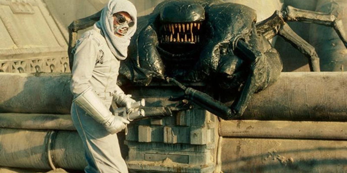 Seorang astronot memegang teropong dengan alien berdiri di belakangnya di Dunia Terlarang