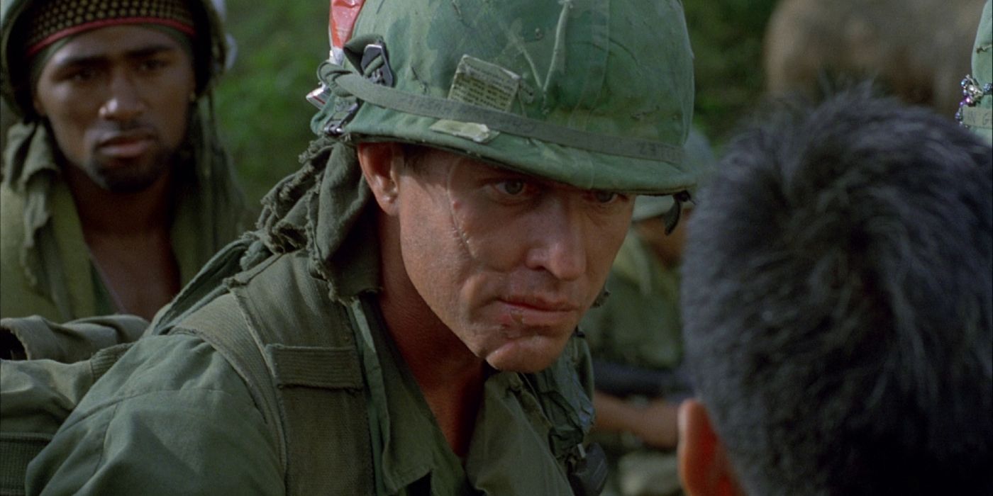 Cuplikan layar dari Peleton 1986. Tom Berenger sebagai Sersan Barnes menginterogasi seorang penduduk desa Vietnam sementara tentara lain melihat di latar belakang.